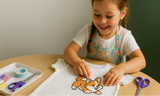 Child wearing an apron, working on a t-shirt with a pressable cartoon dog design at a table.